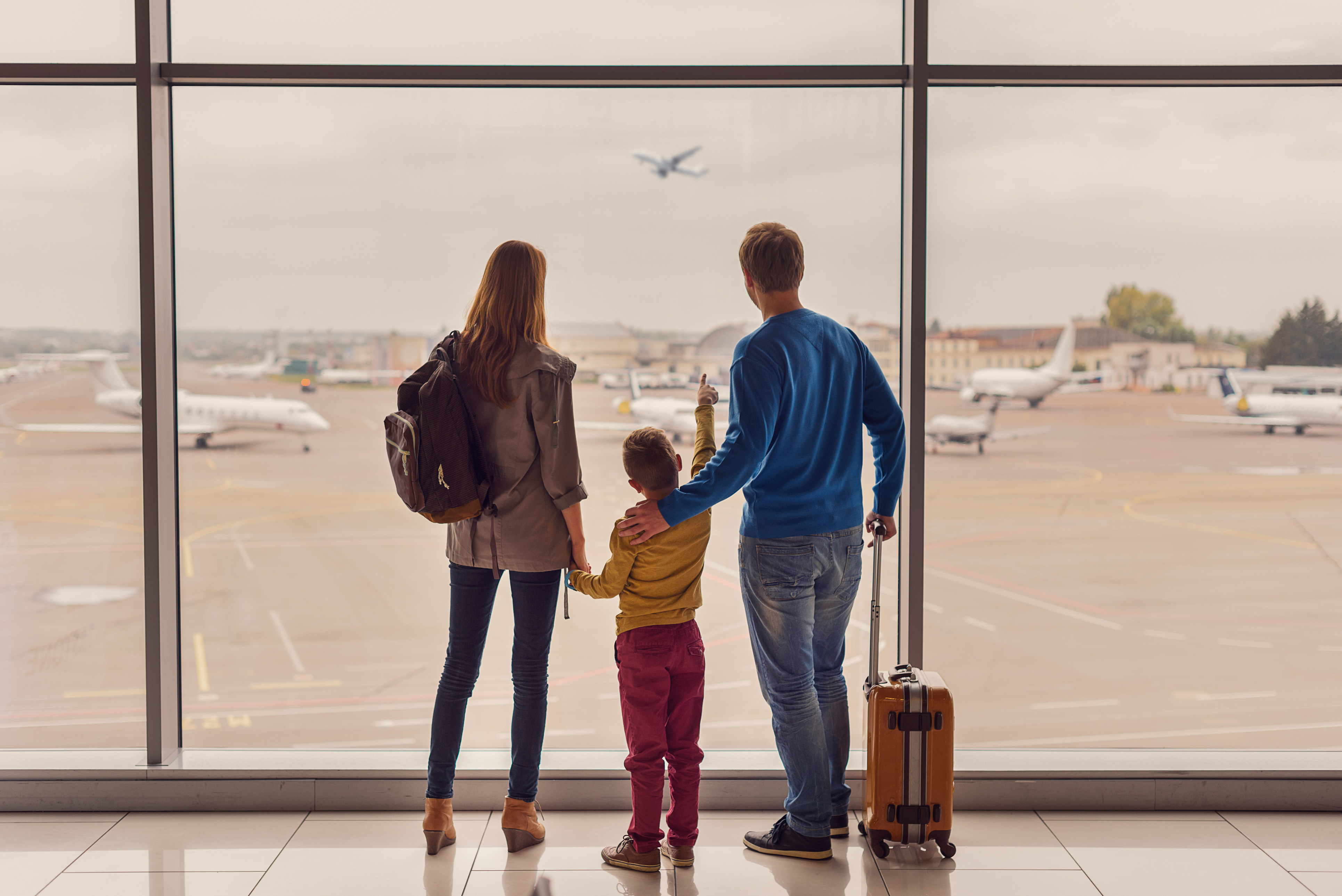 Family of three looking out the airport window at an airplane