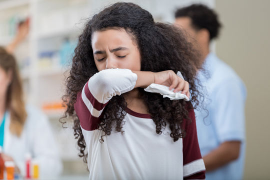 Teenage girl sneezes into her elbow