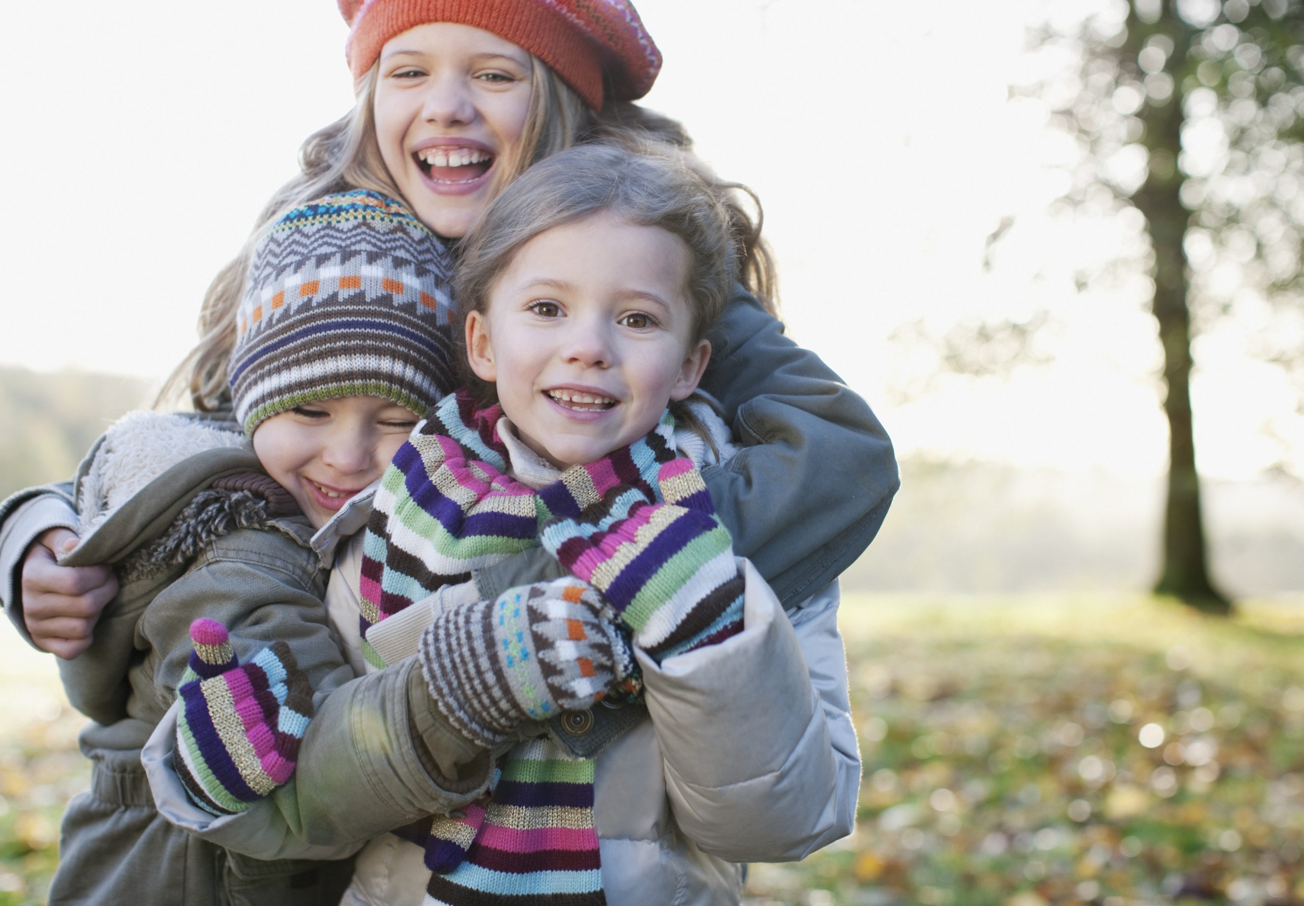 Three siblings with winter hats on playing outside