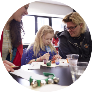 A child and two child life experts joyfully crafting at a table, with various art materials scattered around them.