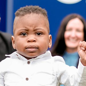 a young boy faces the camera, with his mother smiling in the background