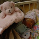 Josie in the NICU with a hat on and a blanket bear near her