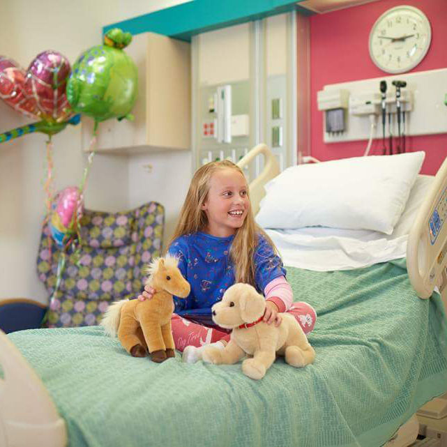 Julia smiling on her hospital bed with stuffed animals