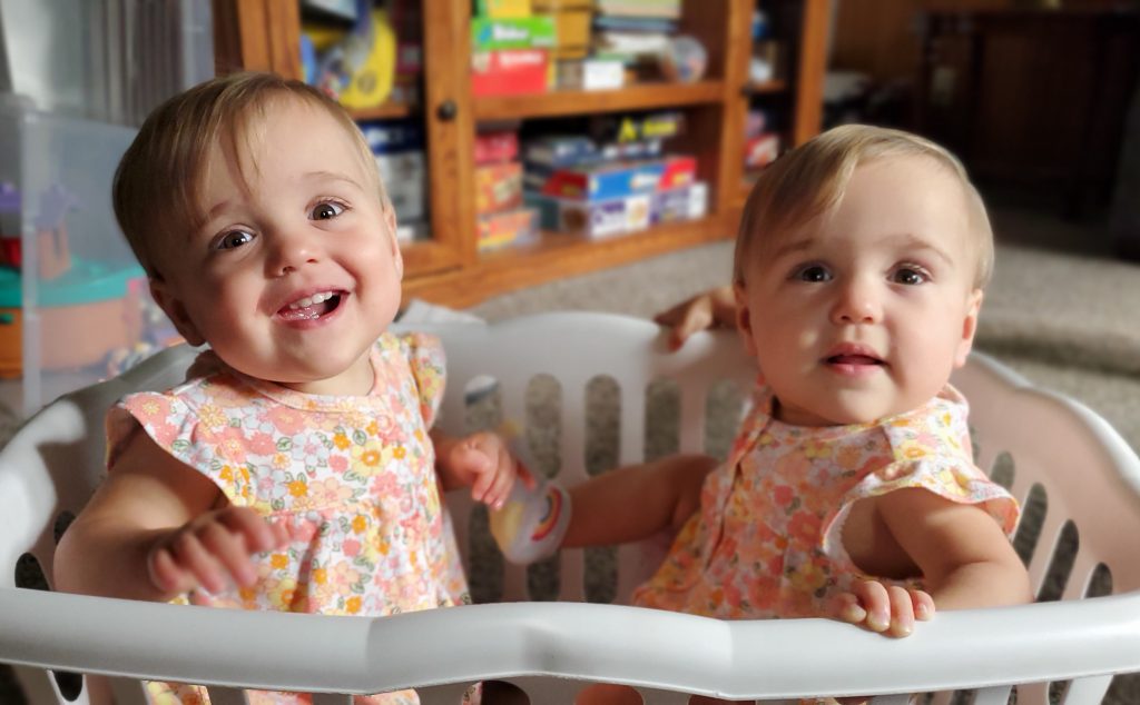 Twin girls Madison and Peyton sitting in a laundry basket and smiling at 1 year old.