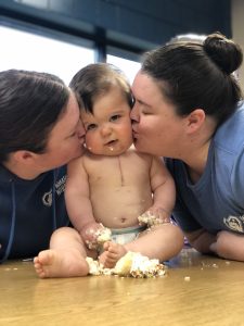 Katie and Betsy kiss William on his cheeks. William's heart transplant scar is visible.
