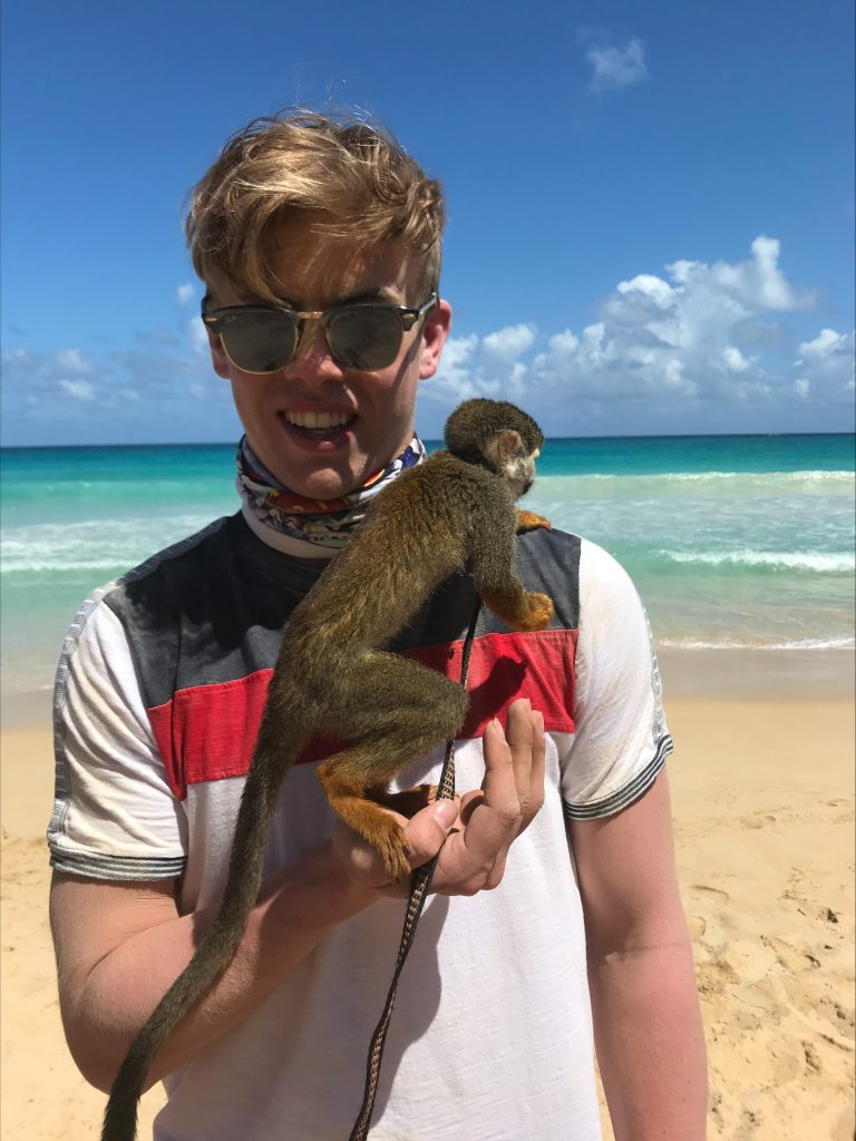 Luke Bonte on a beach with a monkey during his high school senior trip.