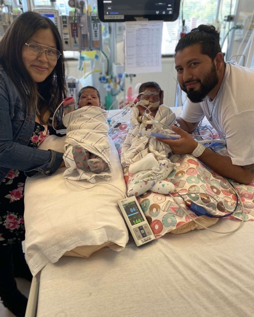Jasmin and Angel holding Luna and Sol who are in the hospital hooked up to machines.