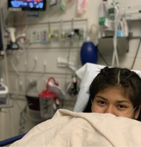 Photo of Marielena, leukemia patient, in a hospital bed, pulling the blanket over her mouth