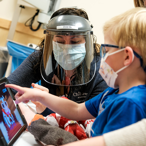 A child life specialist showing a young child games on an iPad for distraction