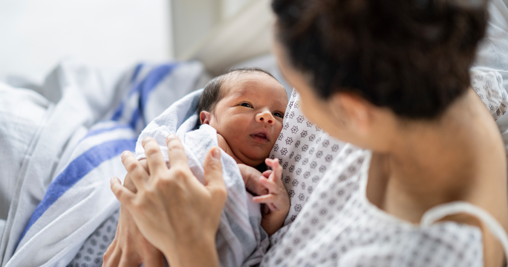 Newborn baby wrapped in blanket with parent in hospital bed