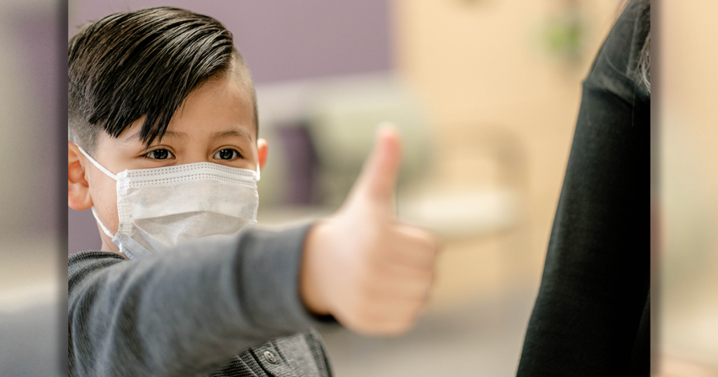 A child in a mask gives a thumbs up