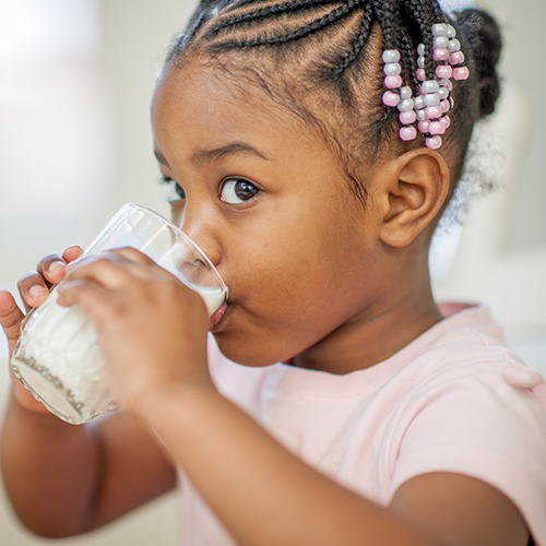 Young girl with braids in her hair drinking milk out of a glass