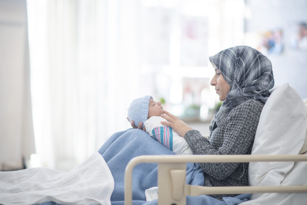A mother wearing a hijab holds her newborn in the hospital