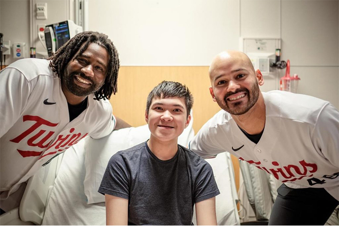 Peter, sitting in a hospital bed smiling at the camera with Twins players next to his side