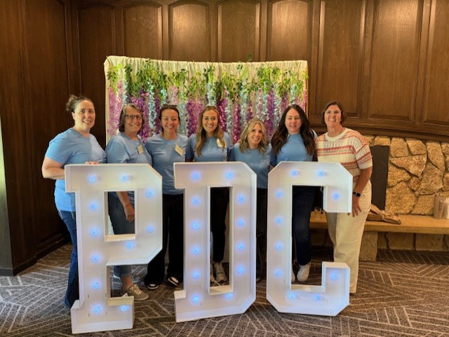 7 people standing behind large letters that say, "PDC"