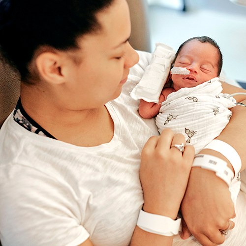 Mom in a chair in the hospital holding her newborn baby in the NICU.