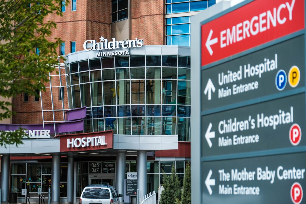 Front of a hospital building, with a sign for Emergency in the foreground