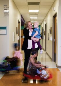 Woman holding young child while two children play at her feet.