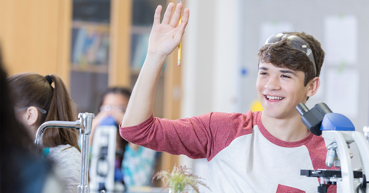 Teen boy raising hand in science class