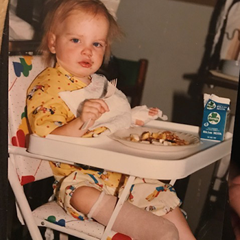 Coley as a child at home eating breakfast in a high chair