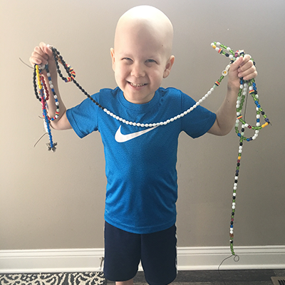 Liam holding up his cancer beads smiling
