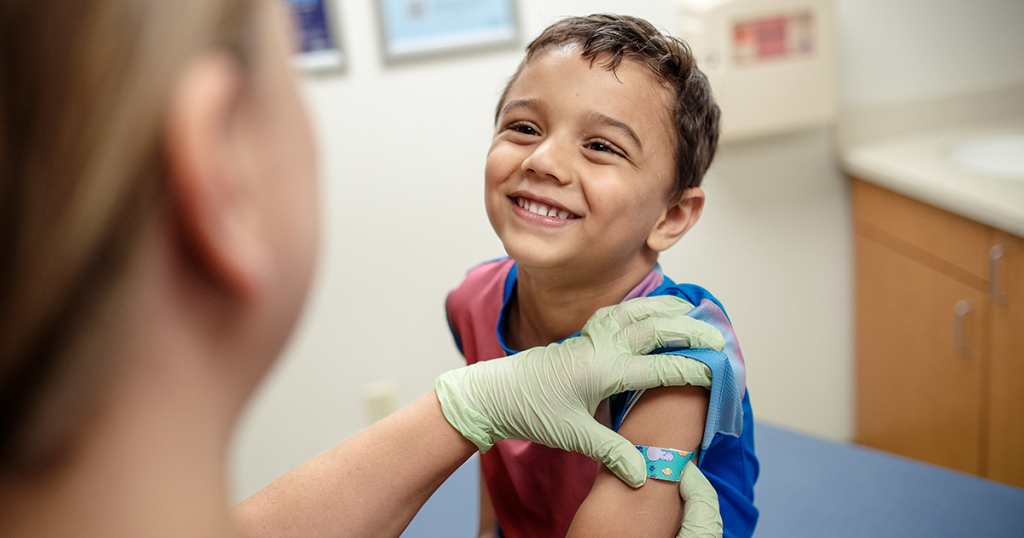 Child smiling with bandage on arm from vaccine