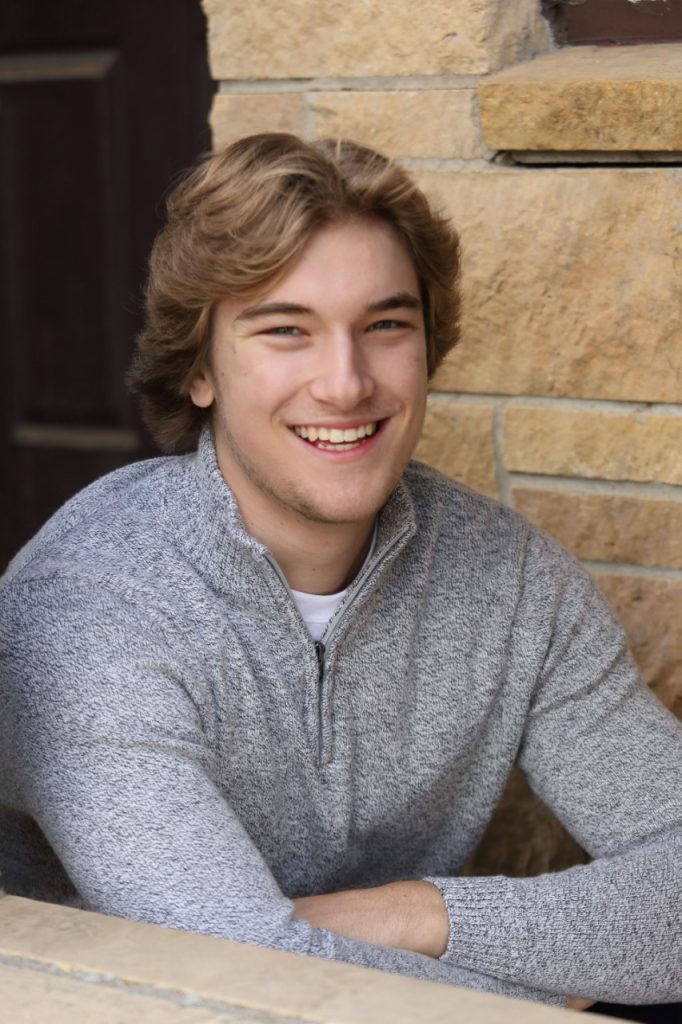 Zander in a grey sweater smiling in front of a brick wall