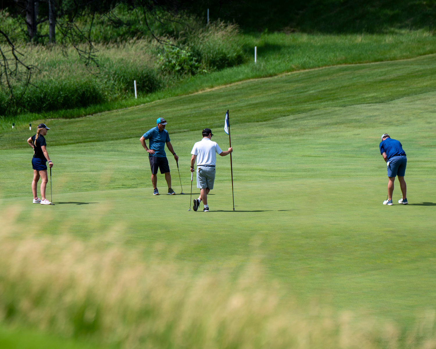 Golfer putting while one holds flag and two others look on